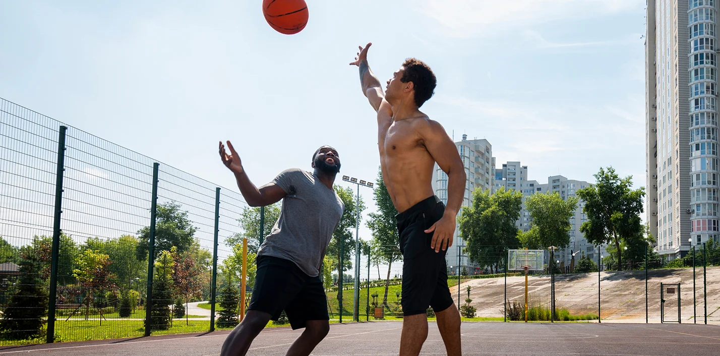 Two men playing basketball outdoors on a sunny court