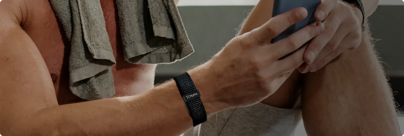 Person resting after exercise with a towel, checking a phone while wearing a knit wellness band